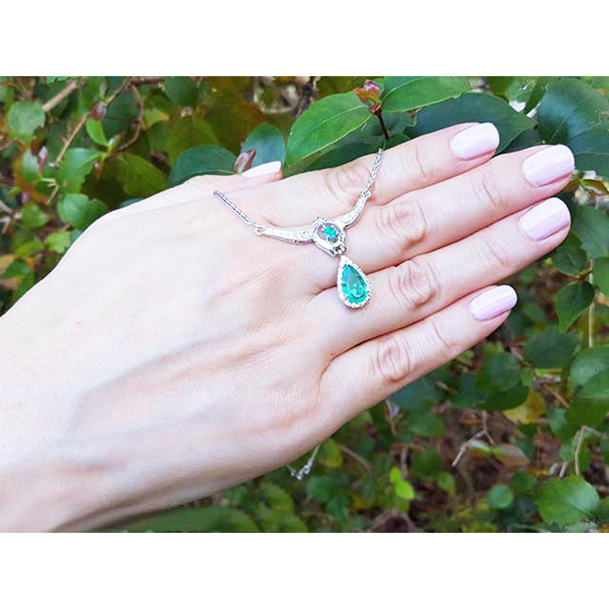 
Hand displaying an authentic Colombian emerald necklace May birthstone pear-shaped against a green leafy background