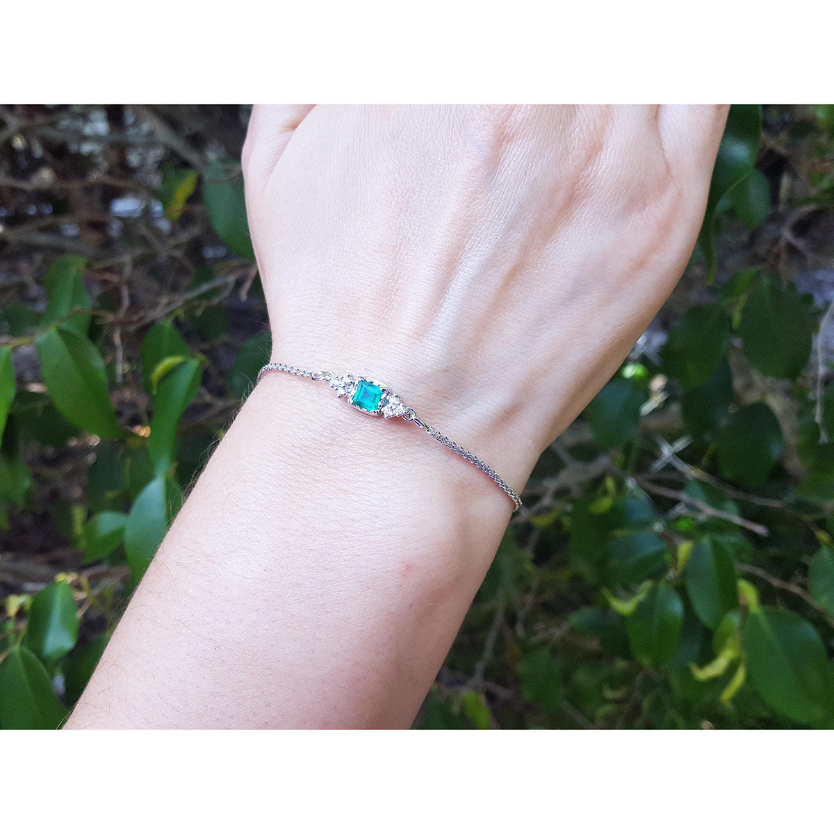 Hand wearing a bracelet with a colombian emerald against a natural background.