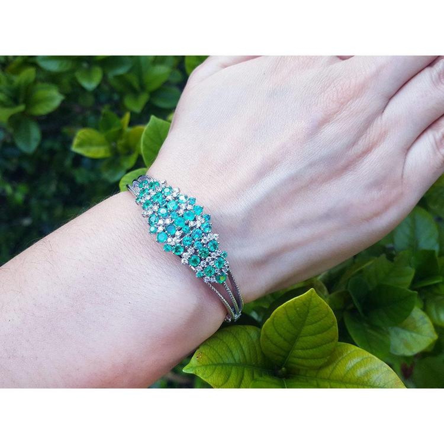 14k white gold bangle bracelet with prong-set round Colombian emeralds and natural diamonds on a wrist.