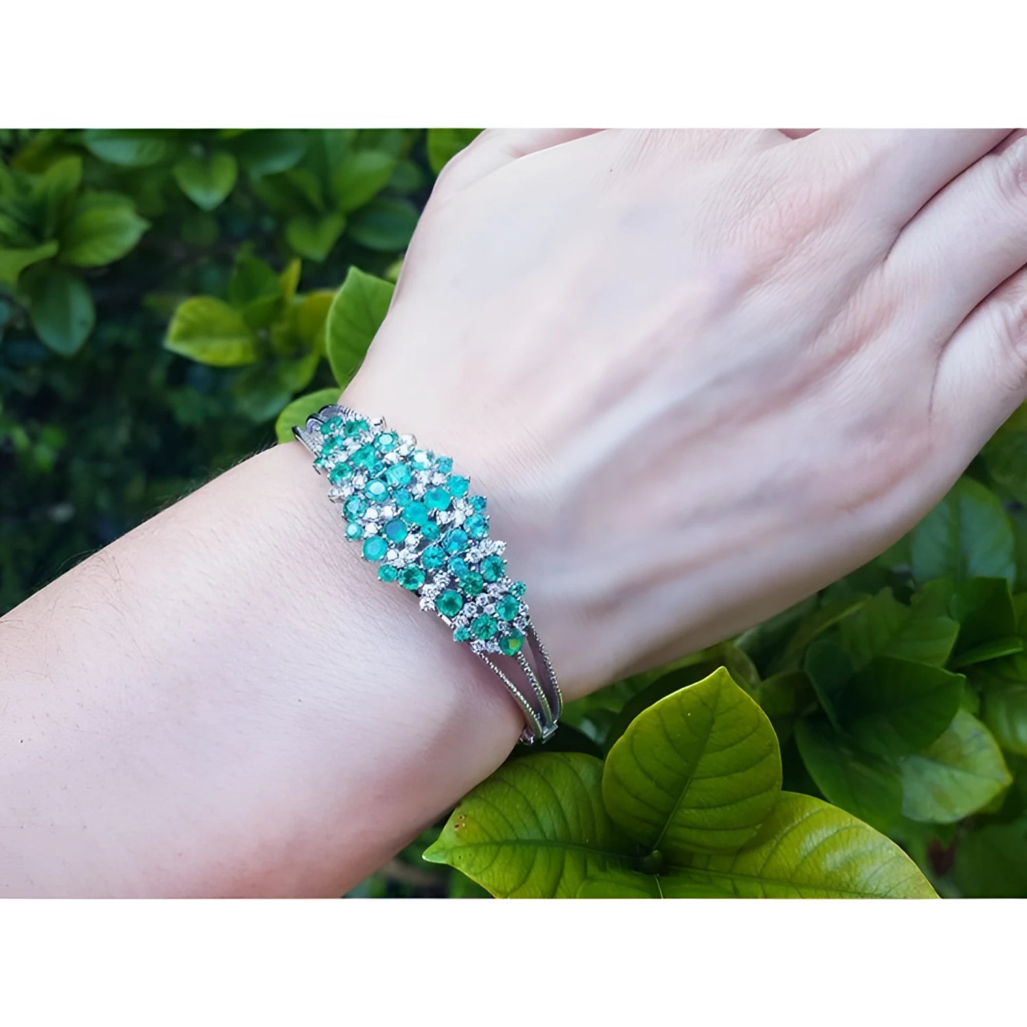 14k white gold bangle bracelet with prong-set round Colombian emeralds and natural diamonds on a wrist.