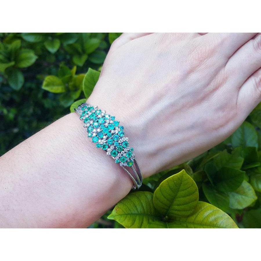 14k white gold bangle bracelet with prong-set round Colombian emeralds and natural diamonds on a wrist.