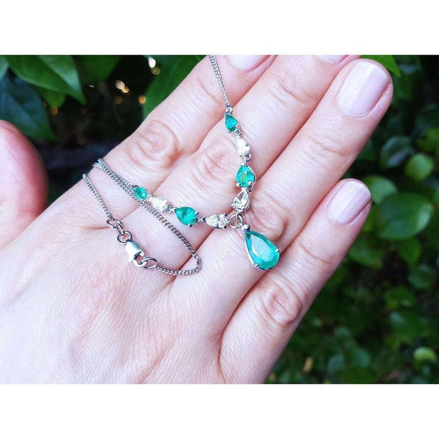 14k white gold necklace with pear-shaped emeralds and diamonds on a hand.