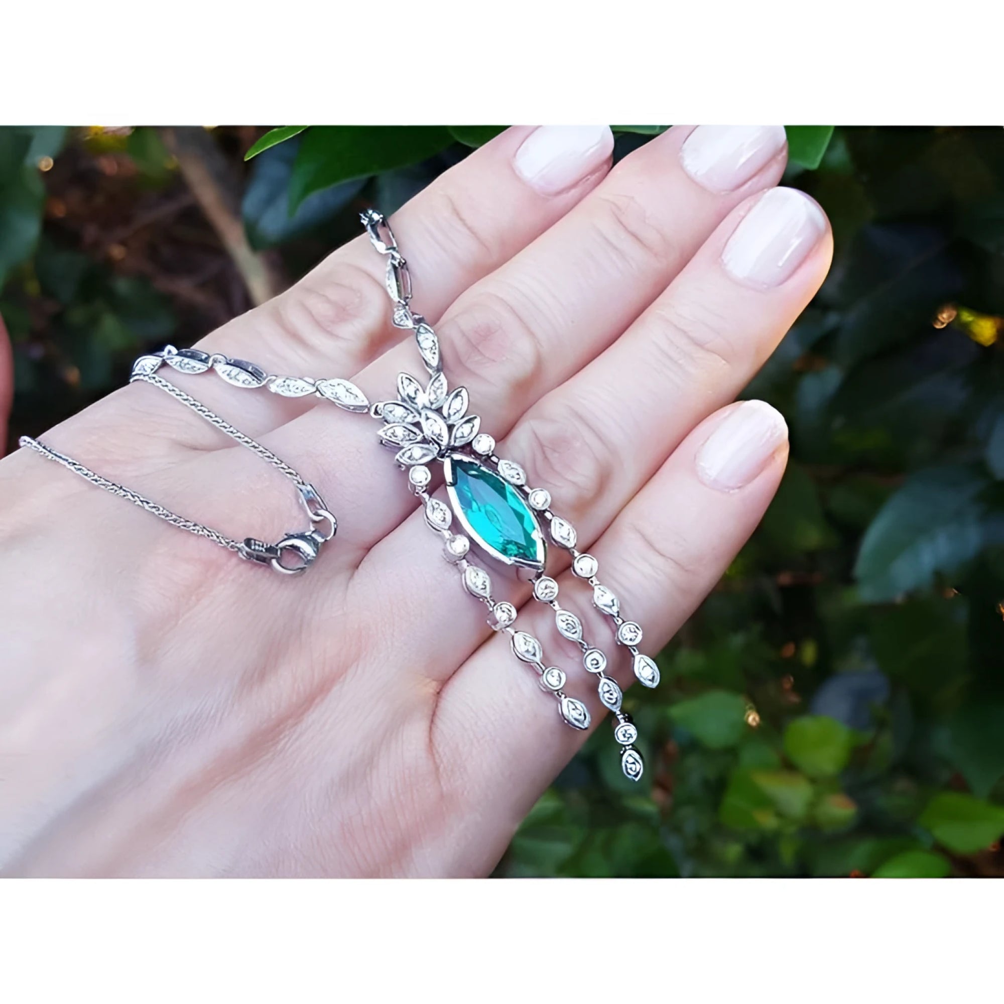 Marquise Colombian emerald and diamond necklace in 14K white gold, held in a hand.