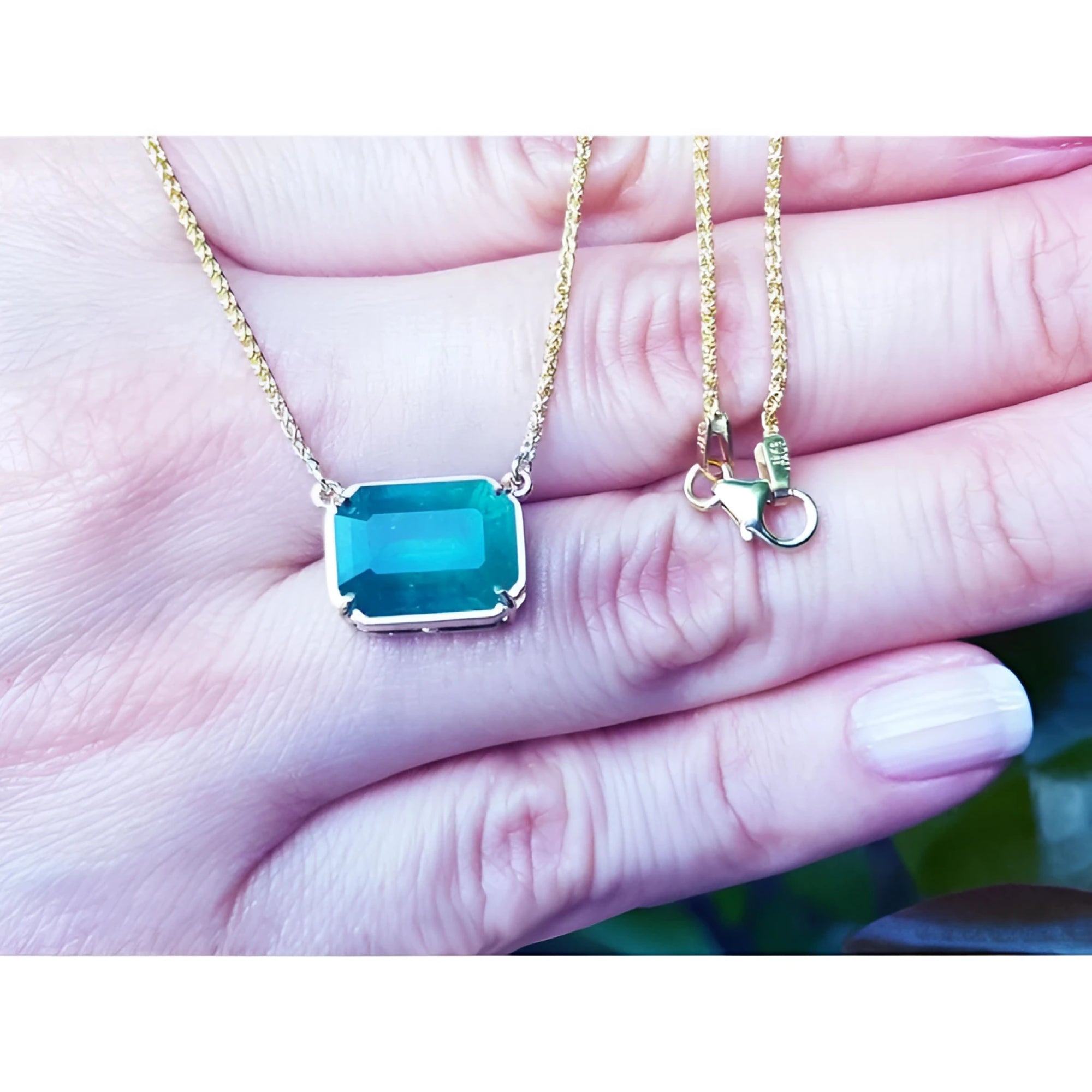 Emerald-cut Colombian emerald solitaire necklace in 18K yellow gold, held in a hand.