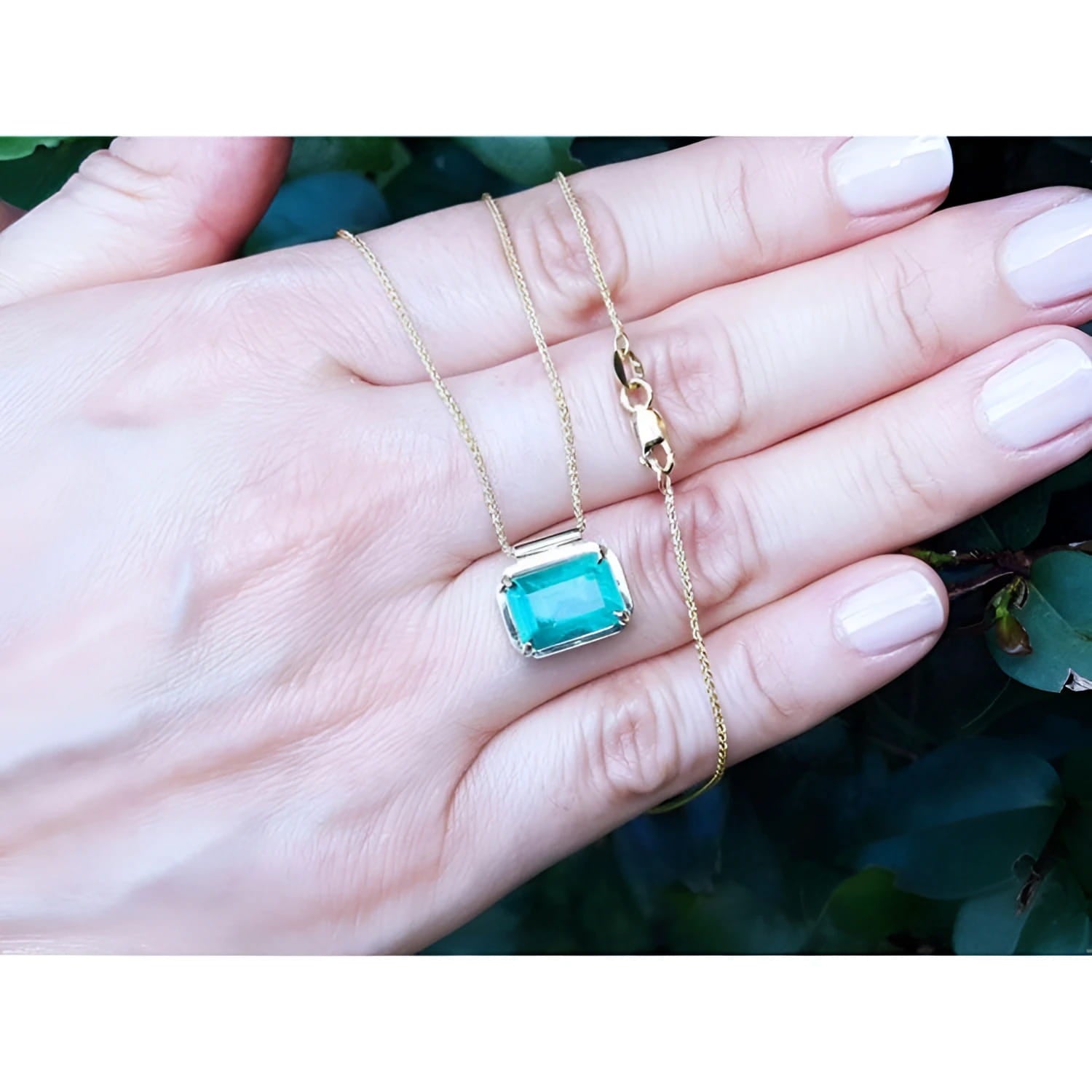 Deep green emerald solitaire necklace in 18K yellow gold, held in a hand.