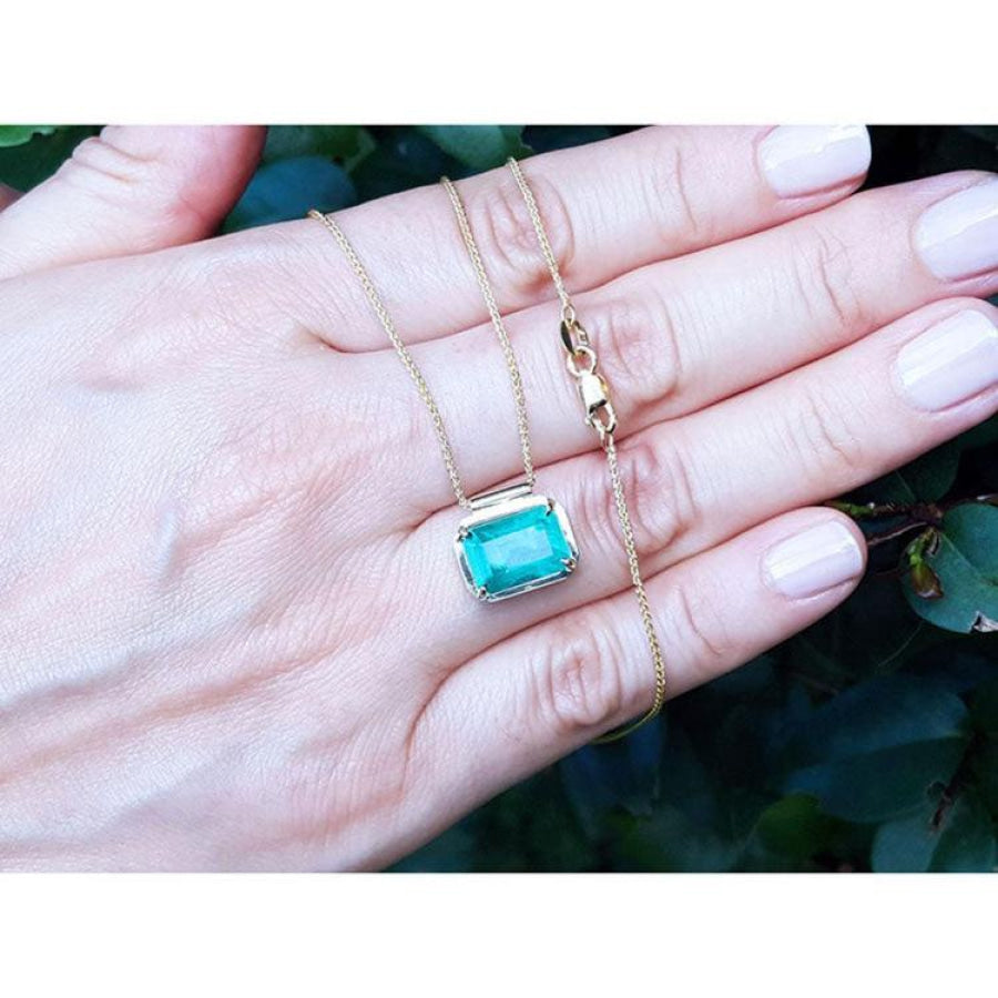 Deep green emerald solitaire necklace in 18K yellow gold, held in a hand.