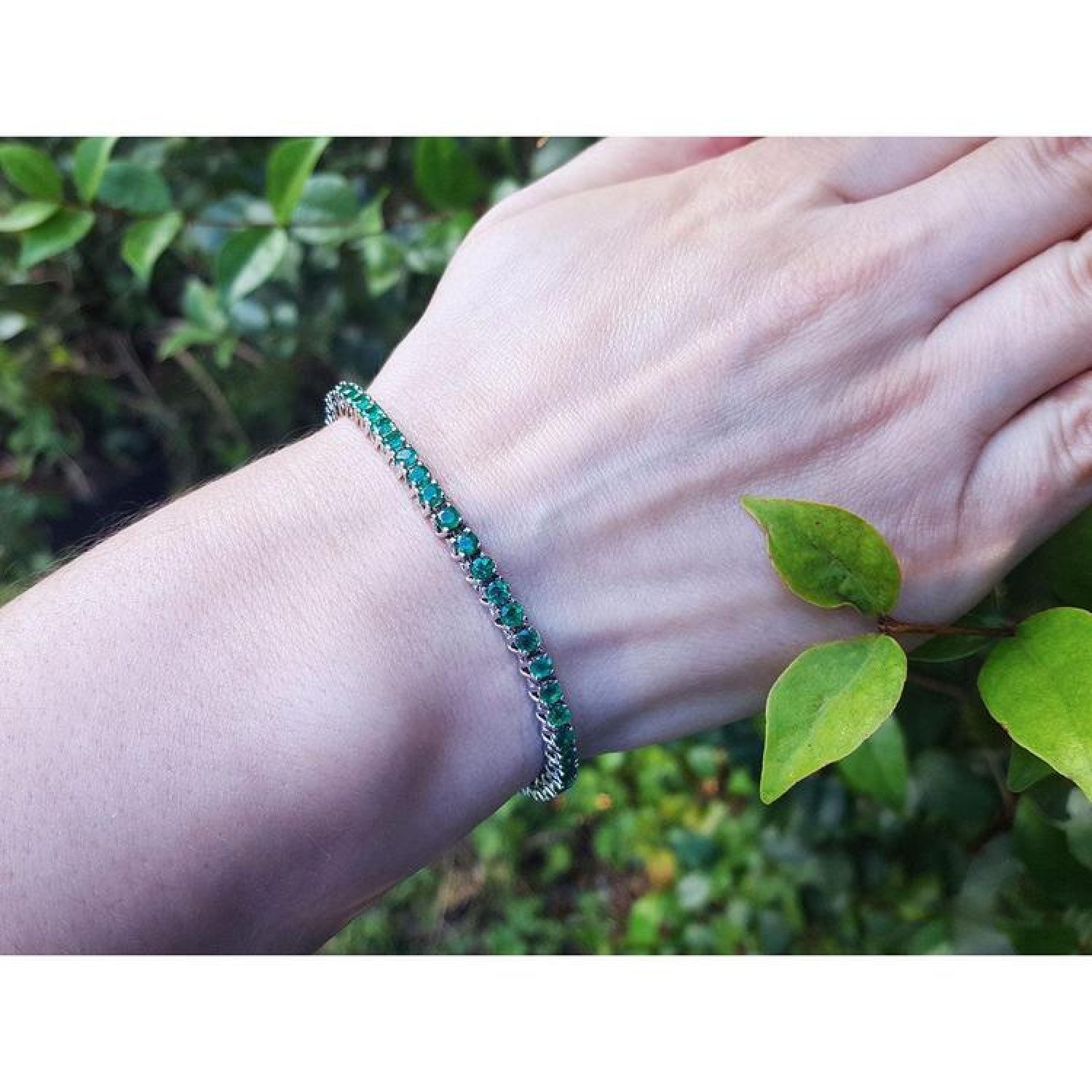 Natural Colombian emeralds tennis bracelet, round cut, prong set in 14K gold, on a wrist.