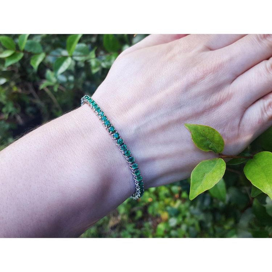Natural Colombian emeralds tennis bracelet, round cut, prong set in 14K gold, on a wrist.