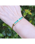 Gold bracelet with real colombian emeralds on a wrist against a green leafy background.