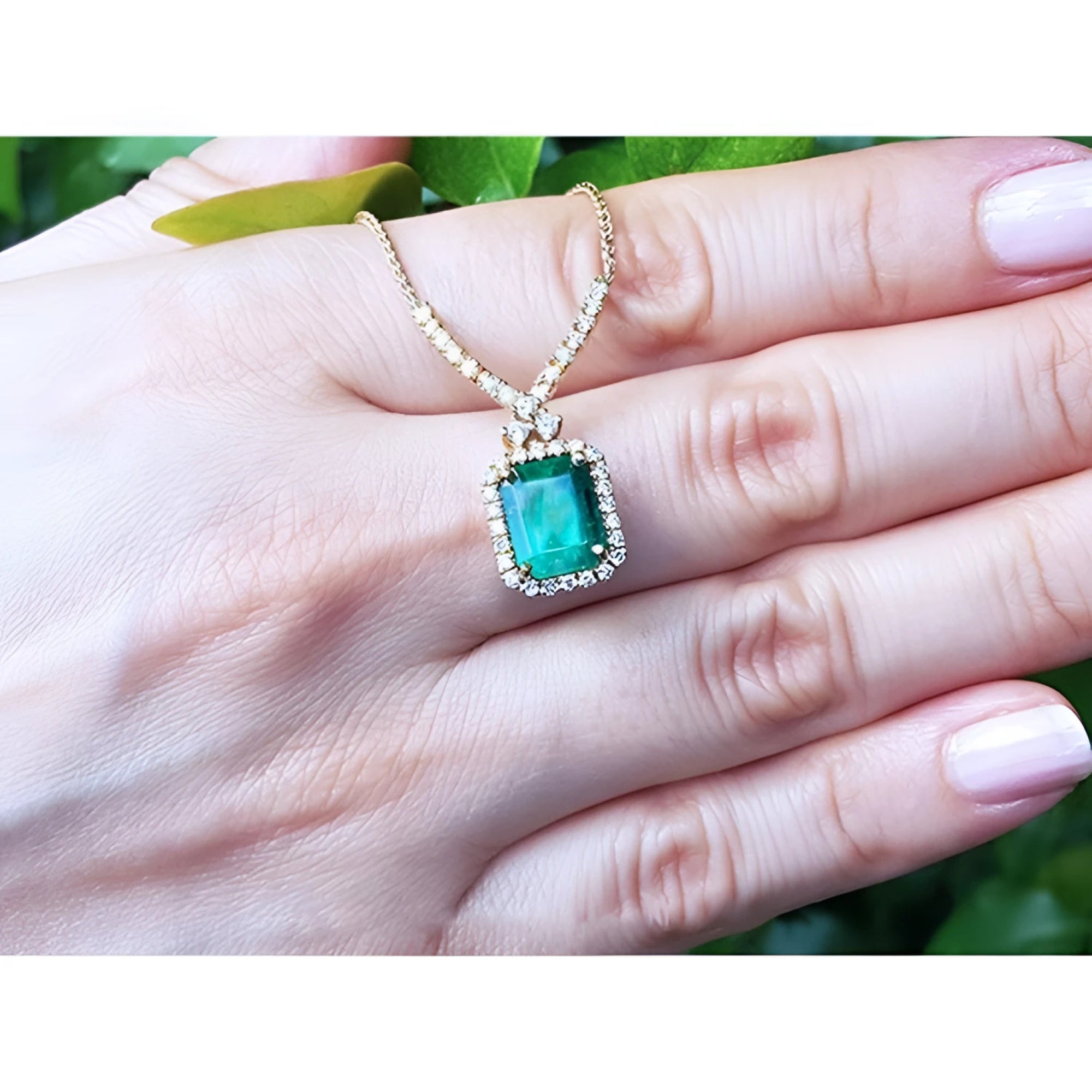Emerald halo necklace with natural diamonds on a 14K yellow gold chain, held by a hand.