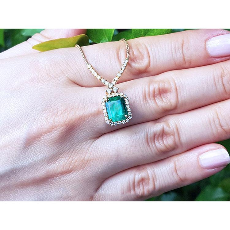 Emerald halo necklace with natural diamonds on a 14K yellow gold chain, held by a hand.