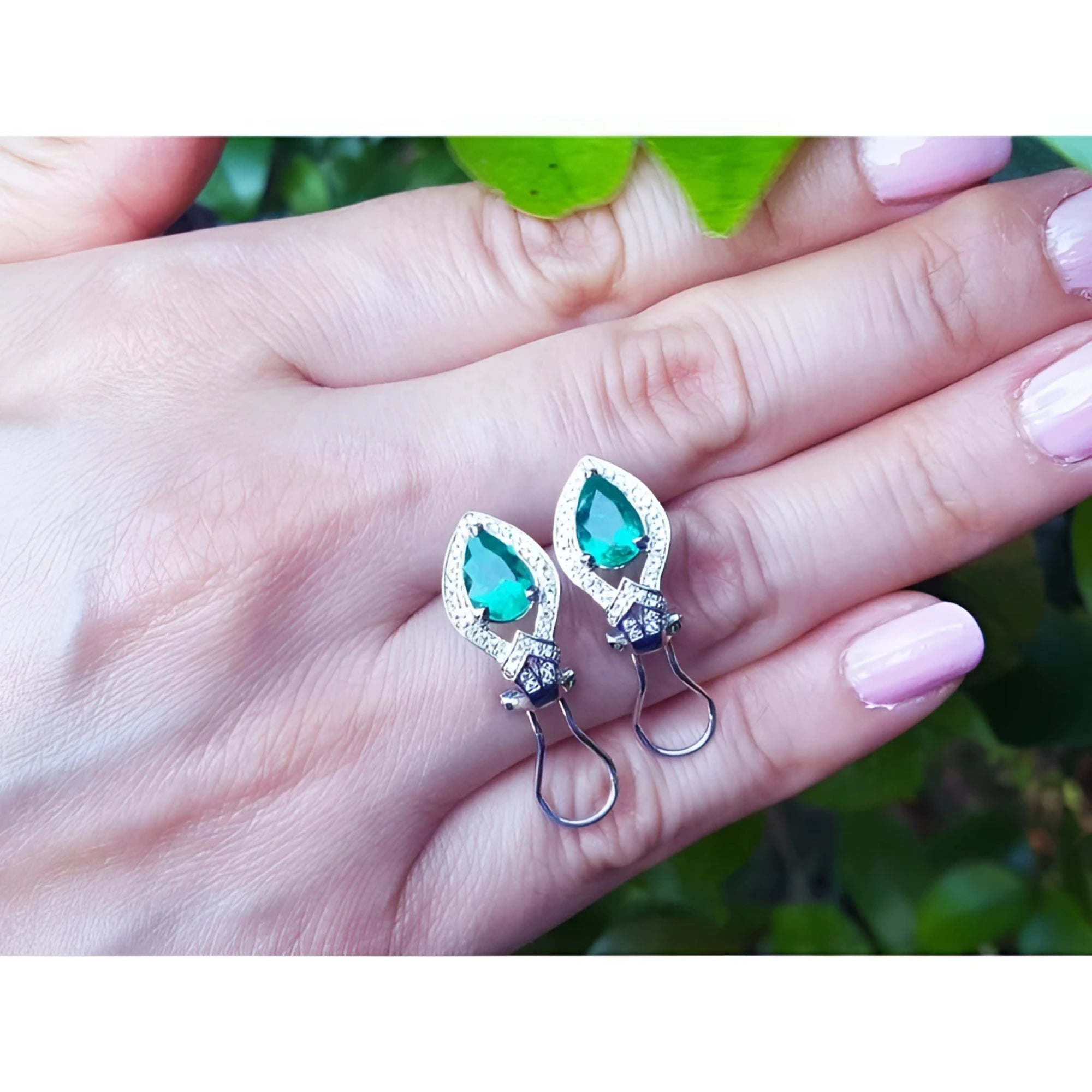 14K white gold clip/post earrings with pear-shaped Colombian emeralds and diamond accents on a hand.