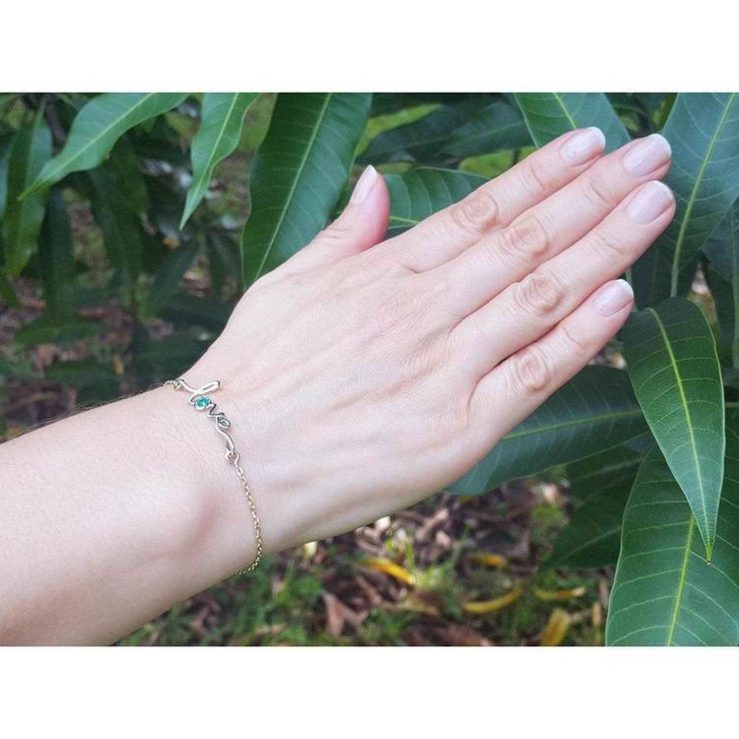 Emerald Love Bracelet in 14K white and yellow gold with a round cut green emerald, worn on a hand.