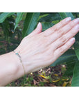 Hand wearing a love bracelet with emerald against a leafy background.