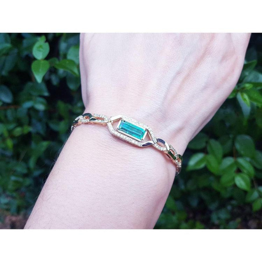 14K yellow gold bracelet with a vibrant emerald-cut Colombian emerald and accent diamonds on a wrist.