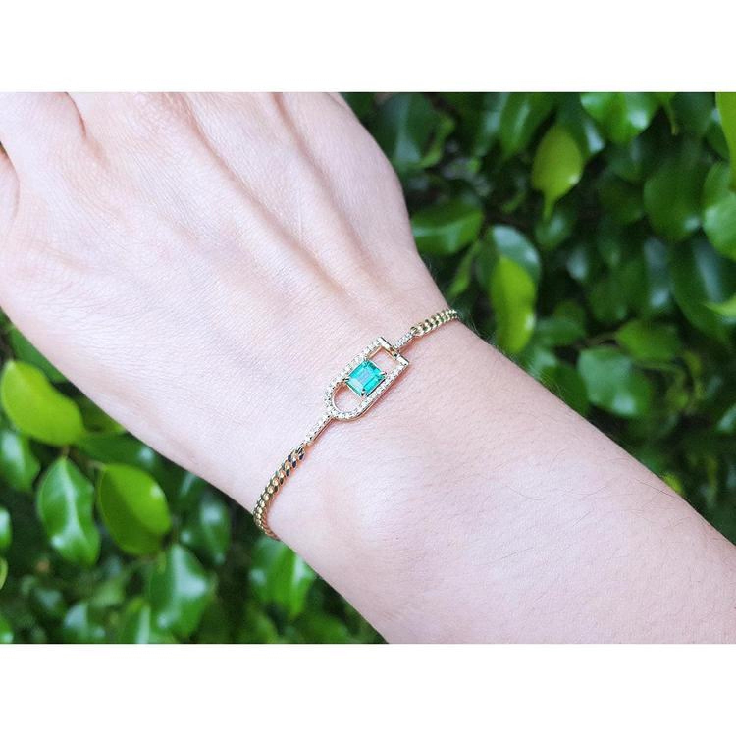 14K yellow gold bracelet with a square emerald-cut Colombian emerald on a woman's wrist.