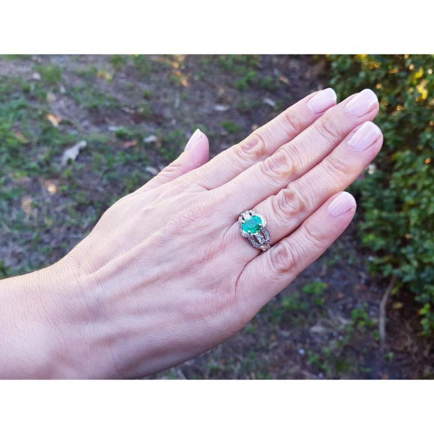 Oval emerald ring in 18K white gold with a decorative bridal band on a hand.