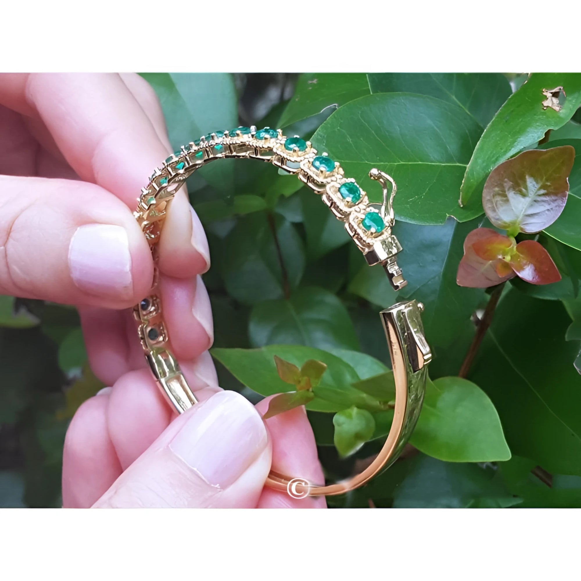 14K gold bangle bracelet with round brilliant cut bluish-green emeralds, prong set in square links.