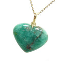 Heart-shaped cabochon emerald stone pendant on a gold chain on its left side view.