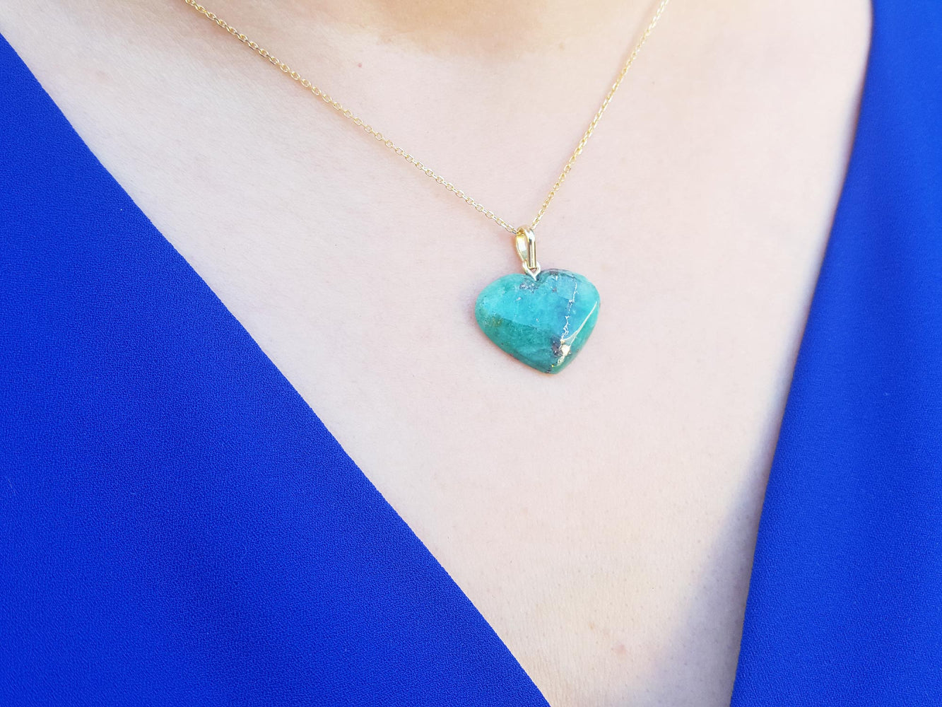 Hand carved emerald heart-shaped pendant on a gold chain worn by a person&#39;s neck.