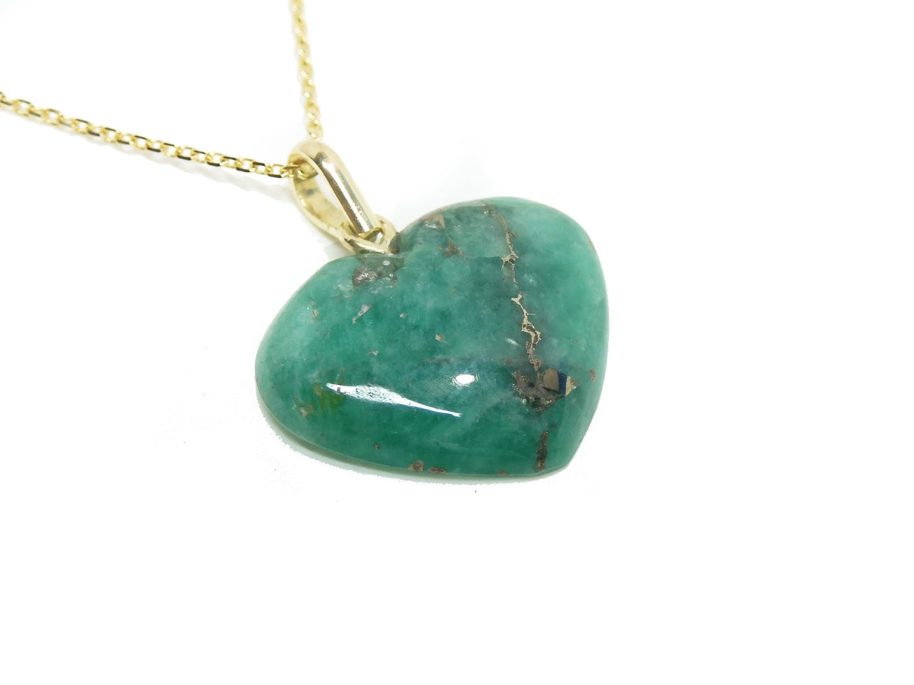 Heart-shaped hand carved emerald pendant on a gold chain against a white background
