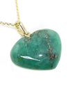 Heart-shaped hand carved emerald pendant on a gold chain against a white background