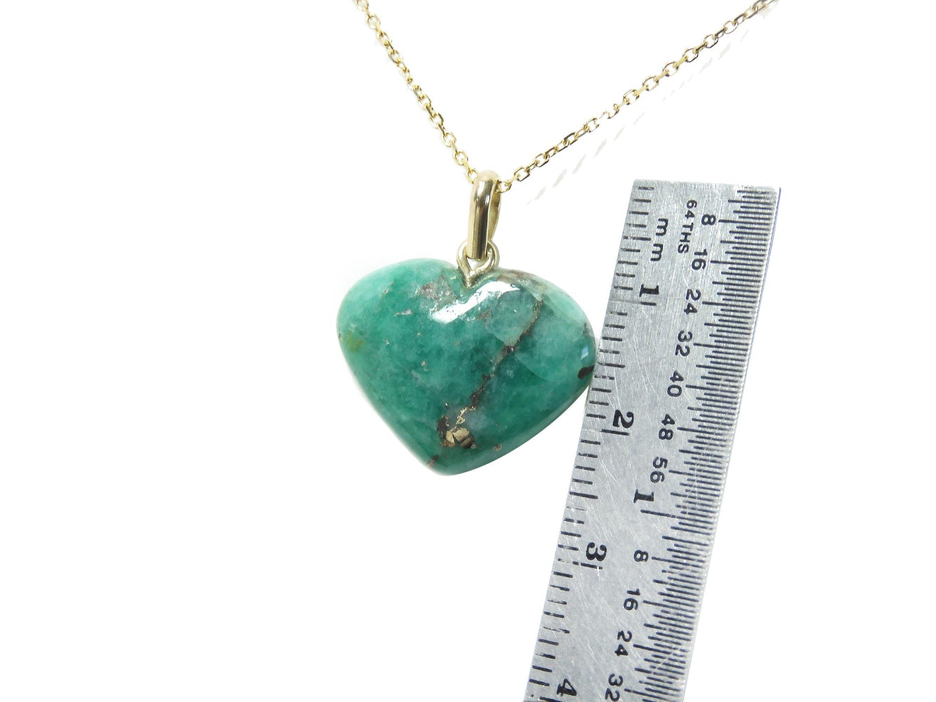 A cabochon hand carved emerald heart-shaped pendant on a gold chain with a ruler for scale.