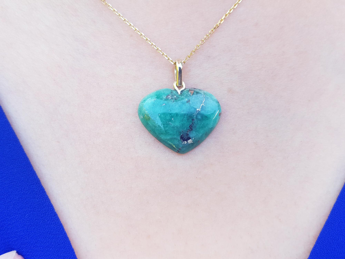 Emerald heart-shaped pendant on a gold chain against a light pink skin background