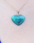 Emerald heart-shaped pendant on a gold chain against a light pink skin background