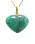 Heart-shaped hand carved emerald cabochon stone pendant on a gold chain on a topside view.