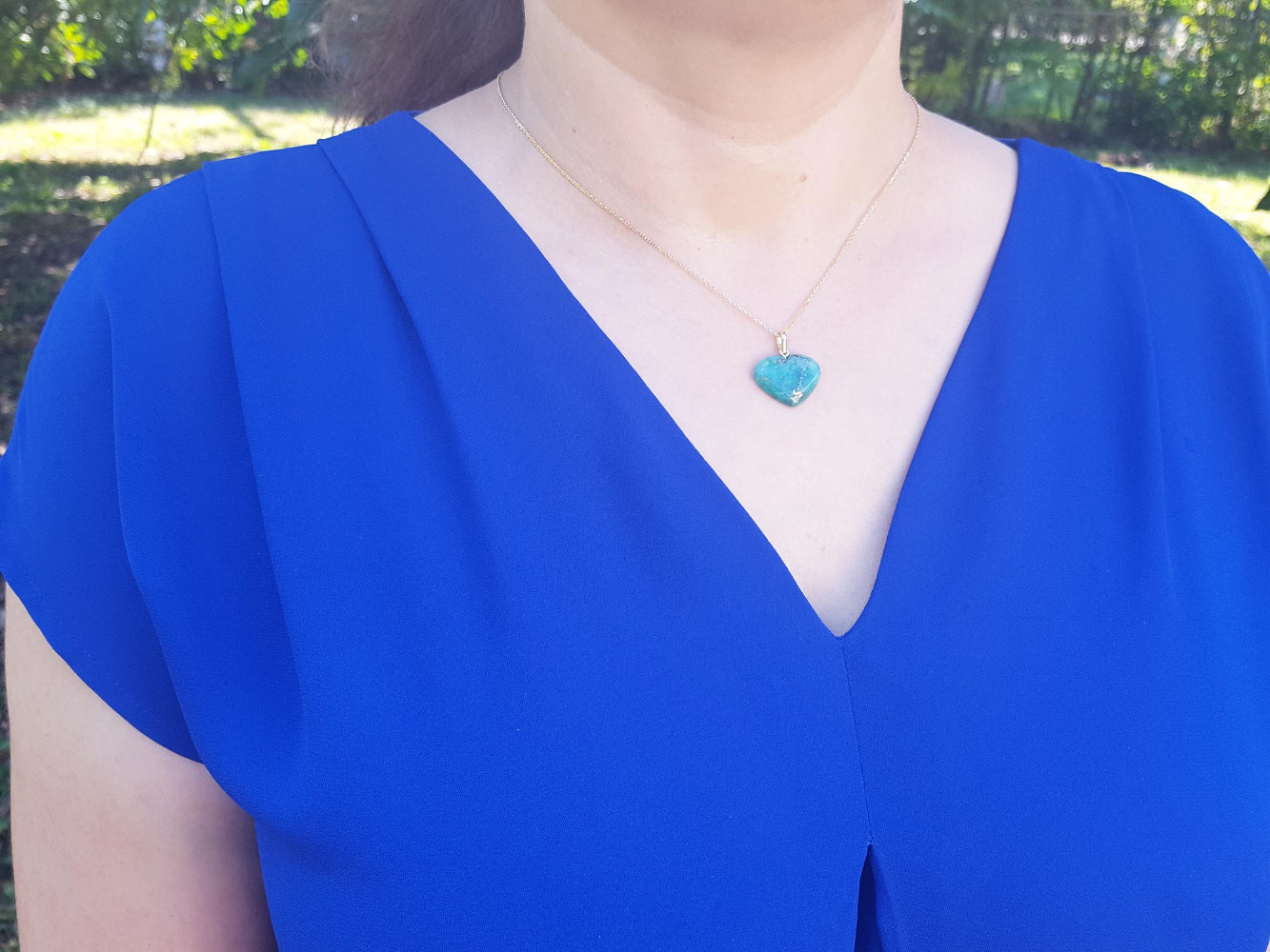 Person wearing a blue dress with a heart-shaped cabochon heart emerald pendant necklace outdoors.