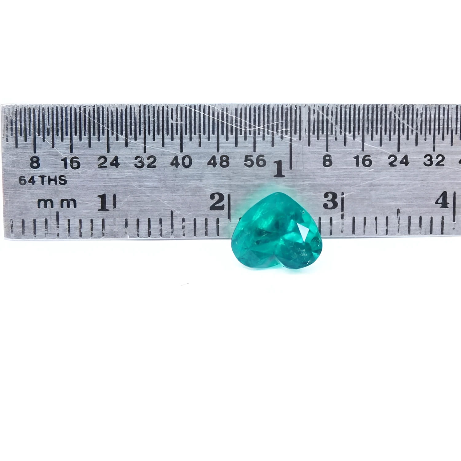 1.26 ct. heart cut Colombian emerald with vibrant bluish-green color, shown next to a ruler for scale.