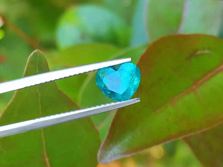 1.26 ct. vibrant bluish-green heart-cut Colombian emerald held by tweezers.