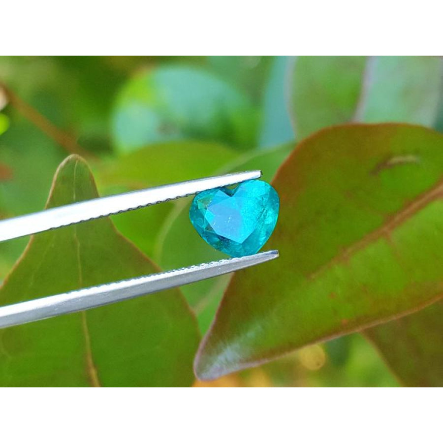 1.26 ct. vibrant bluish-green heart-cut Colombian emerald held by tweezers.