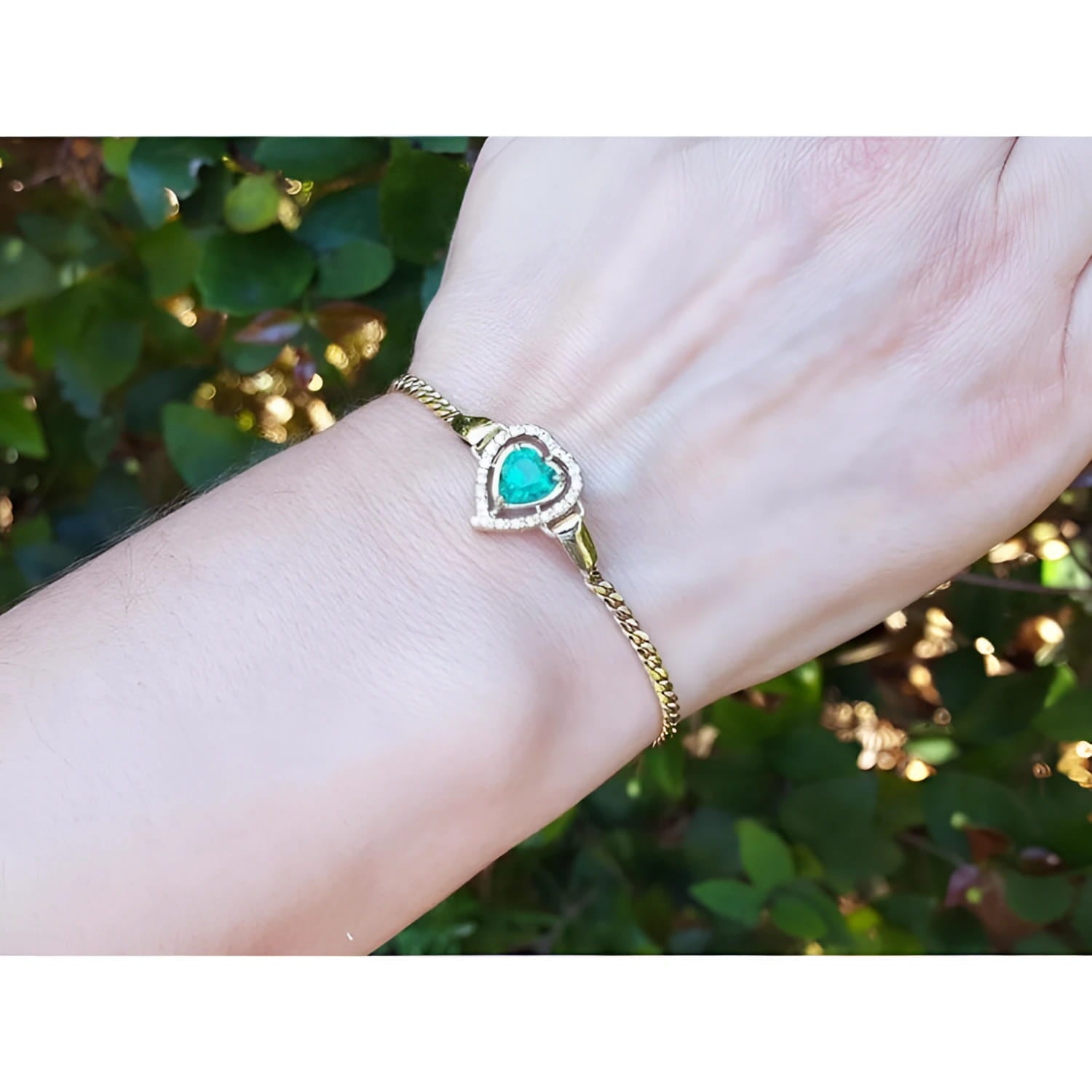 14K yellow gold bracelet with a heart-shaped emerald surrounded by diamonds on a woman's wrist.