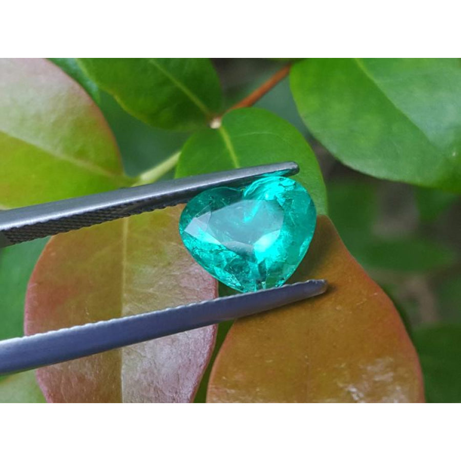 2.54 carat GIA certified heart cut Colombian emerald, sparkling bluish-green, held by tweezers.
