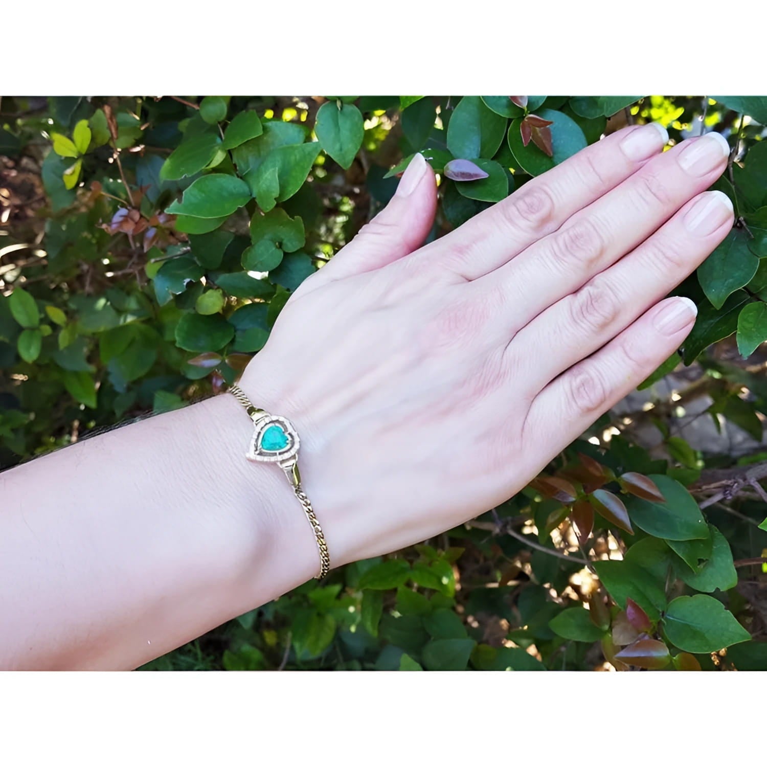 Hand wearing a 14K yellow gold bracelet with a heart-shaped Colombian emerald and diamonds.