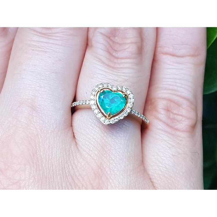 Heart-shaped emerald ring with halo diamond made of 14k yellow gold on a finger.