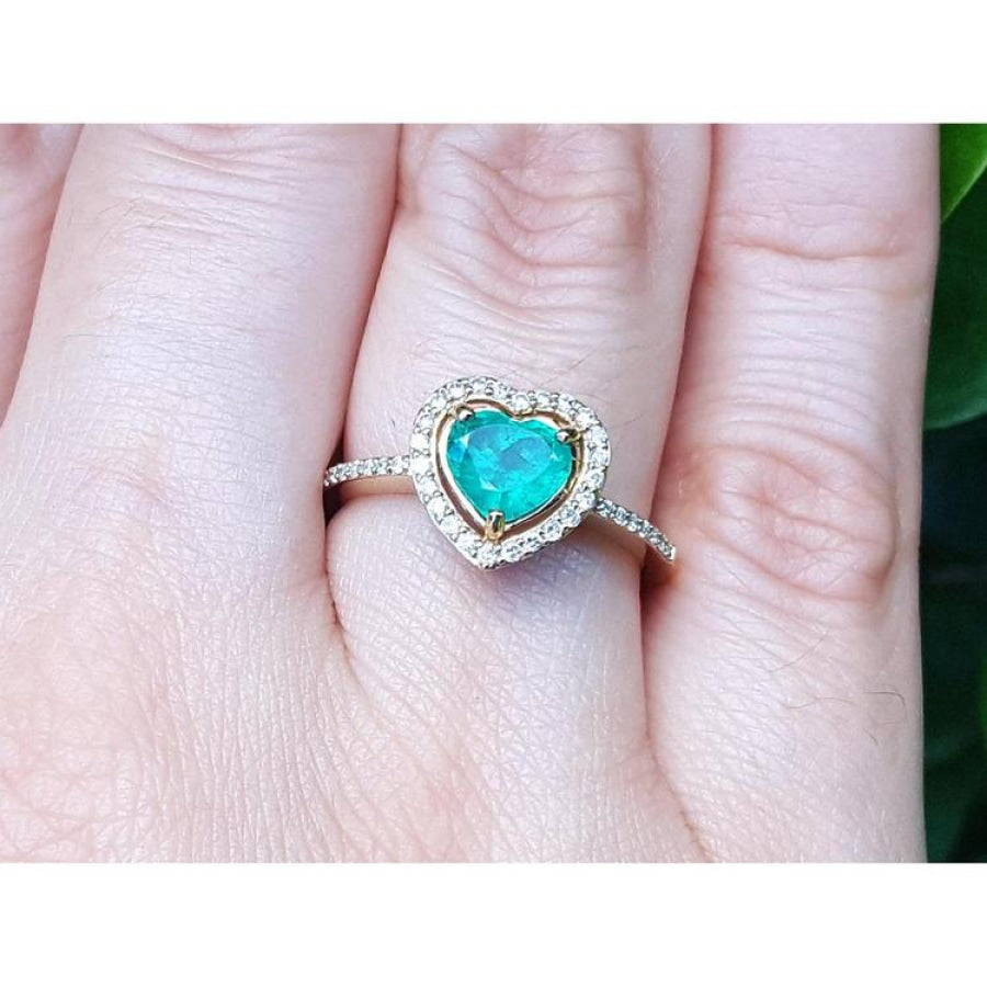 Heart-shaped emerald ring with halo diamond made of 14k yellow gold on a finger.