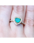 Heart-shaped emerald ring with halo diamond made of 14k yellow gold on a finger.