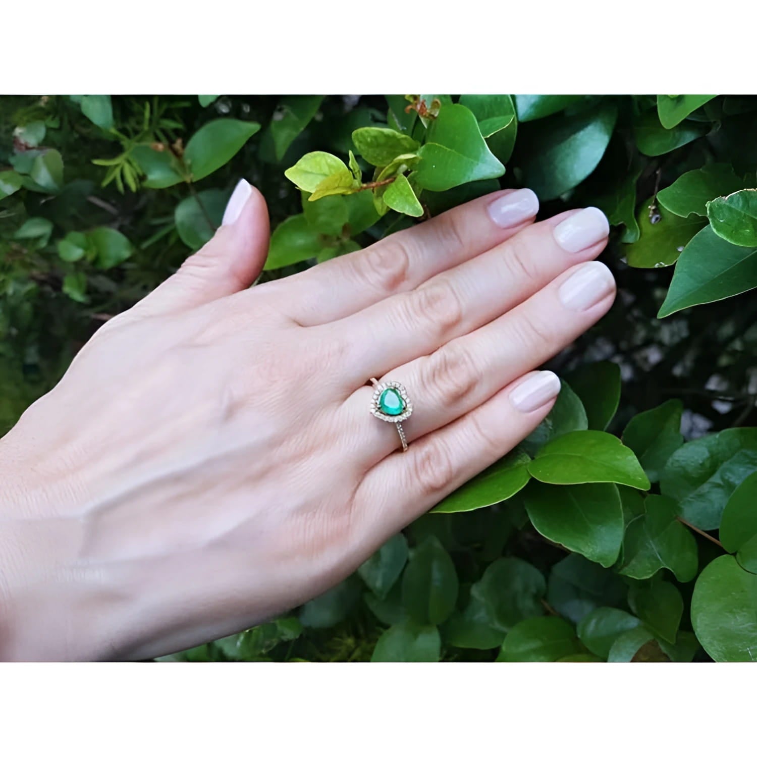 Heart-cut emerald engagement ring with diamond halo on a hand, set in 14K yellow gold.