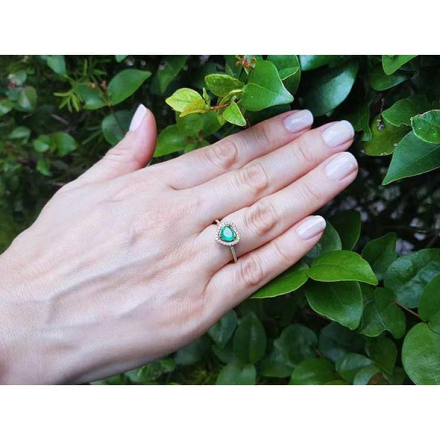 Heart-cut emerald engagement ring with diamond halo on a hand, set in 14K yellow gold.