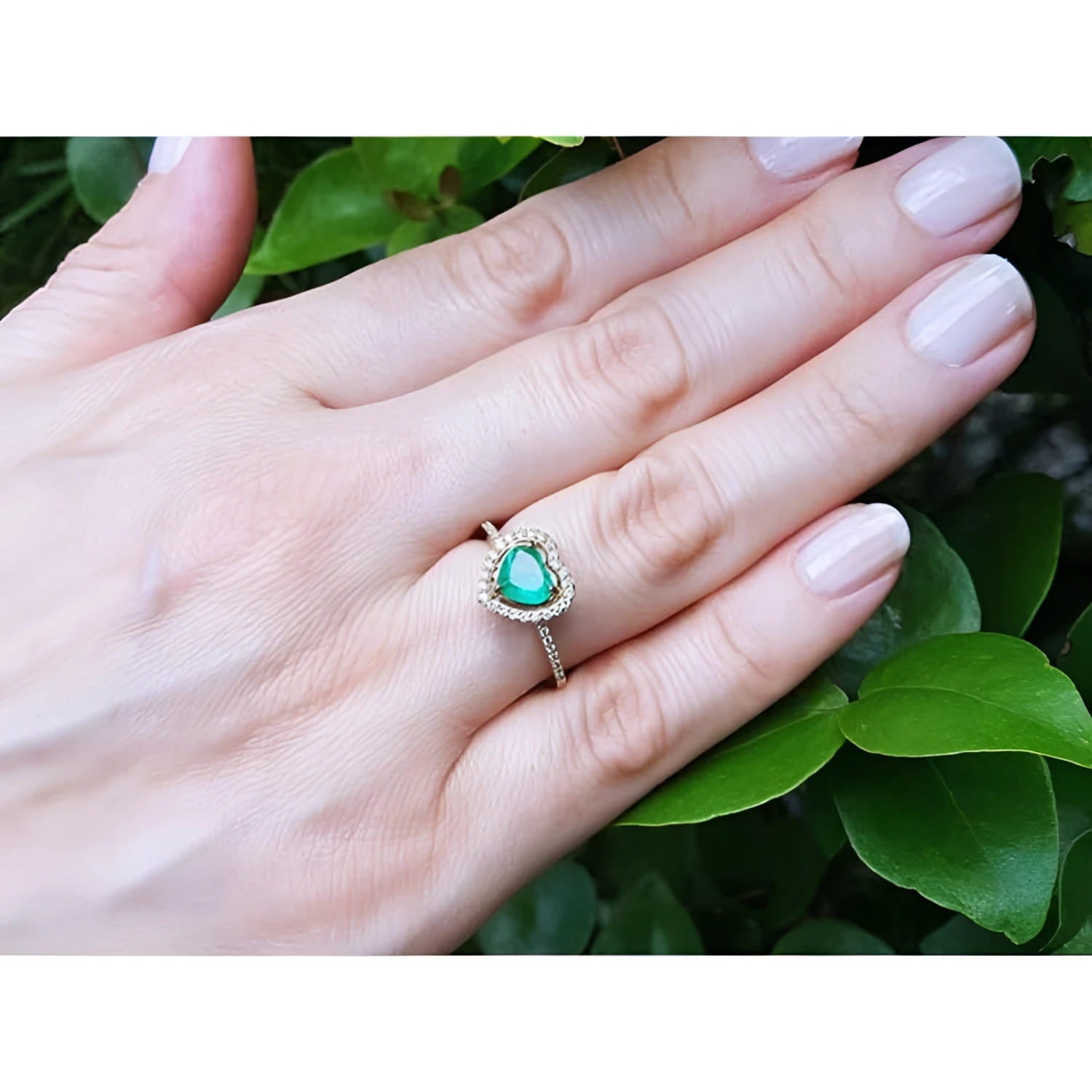 Heart-cut emerald engagement ring with diamond halo on a 14K yellow gold band, worn on a hand.