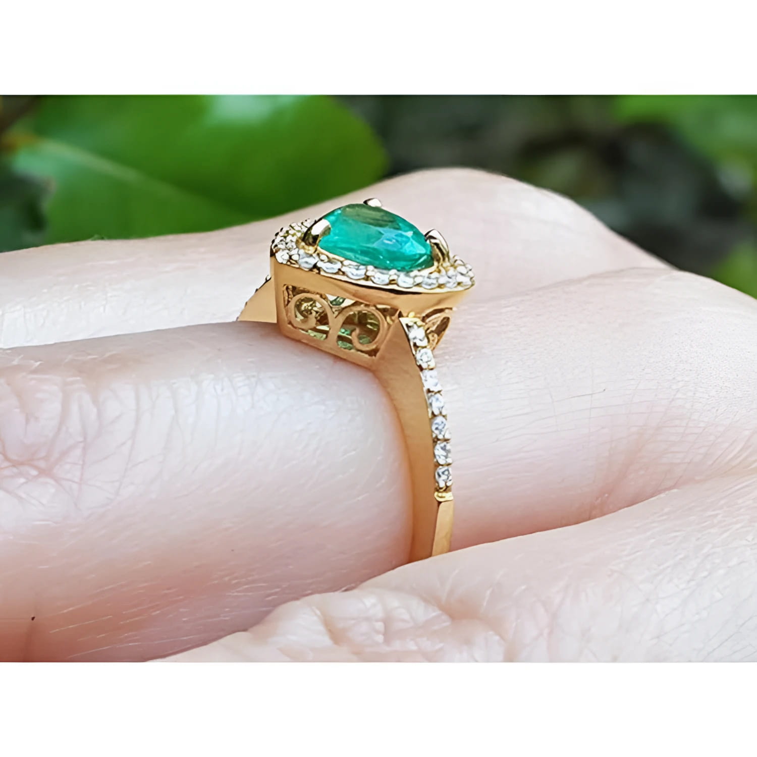 14K yellow gold ring with a heart-cut emerald surrounded by a diamond halo on a hand.