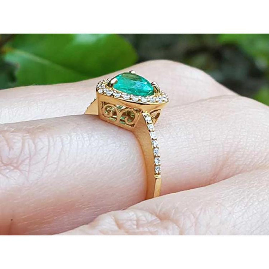 14K yellow gold ring with a heart-cut emerald surrounded by a diamond halo on a hand.