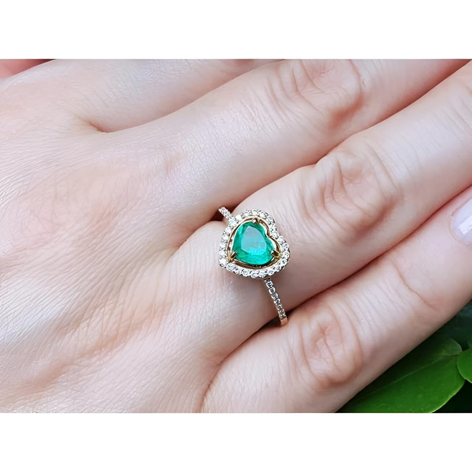 Heart-cut emerald engagement ring with diamond halo on a 14K yellow gold band, worn on a finger.