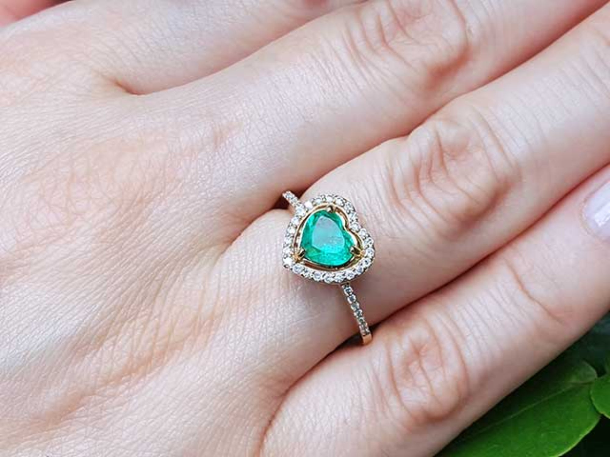 A heart cut emerald engagement ring halo diamonds 14k yellow gold. on a hand.
