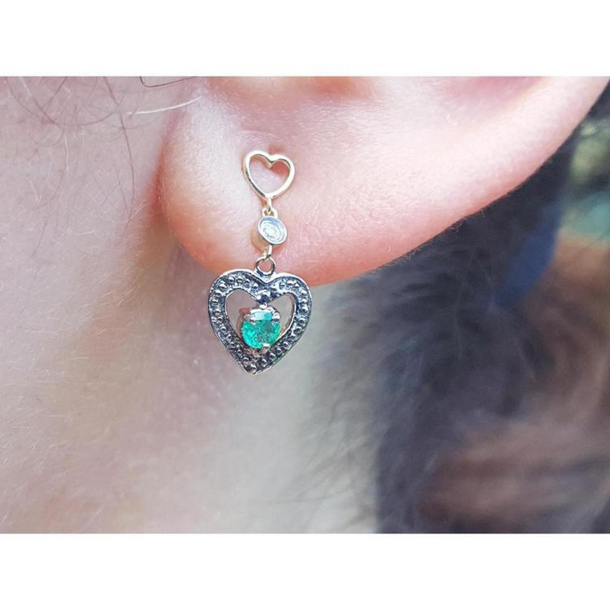 Emerald heart earring made of 14k gold worn on a woman's ear.
