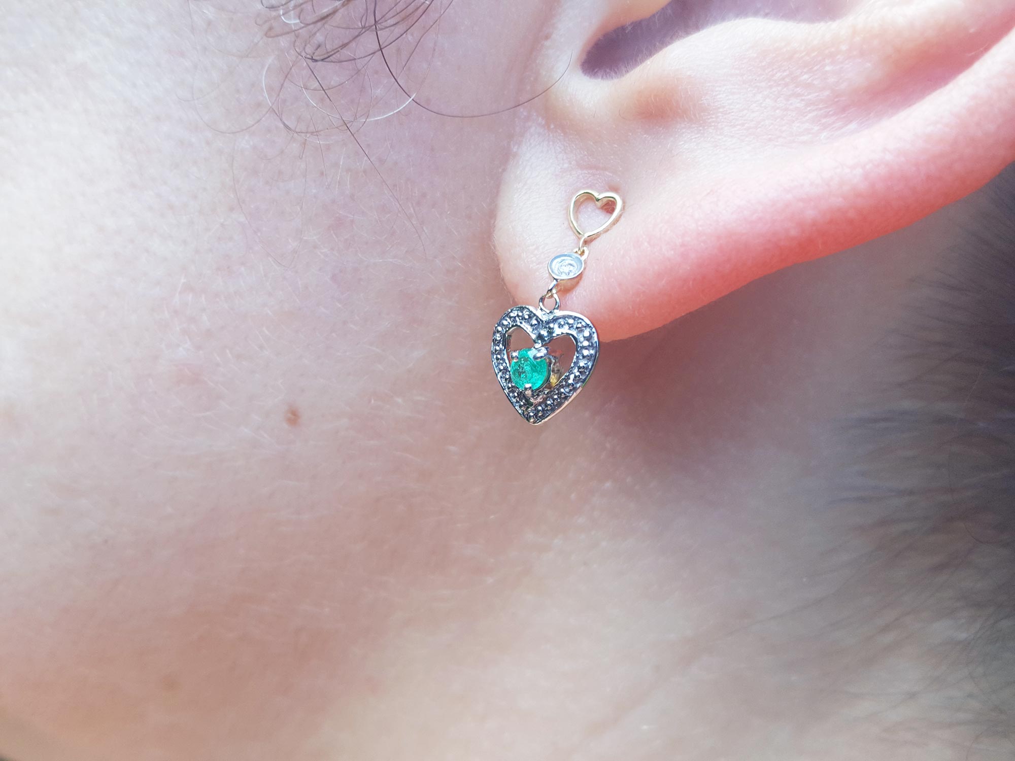 Close-up of a woman&#39;s ear wearing a natural emerald heart earring.