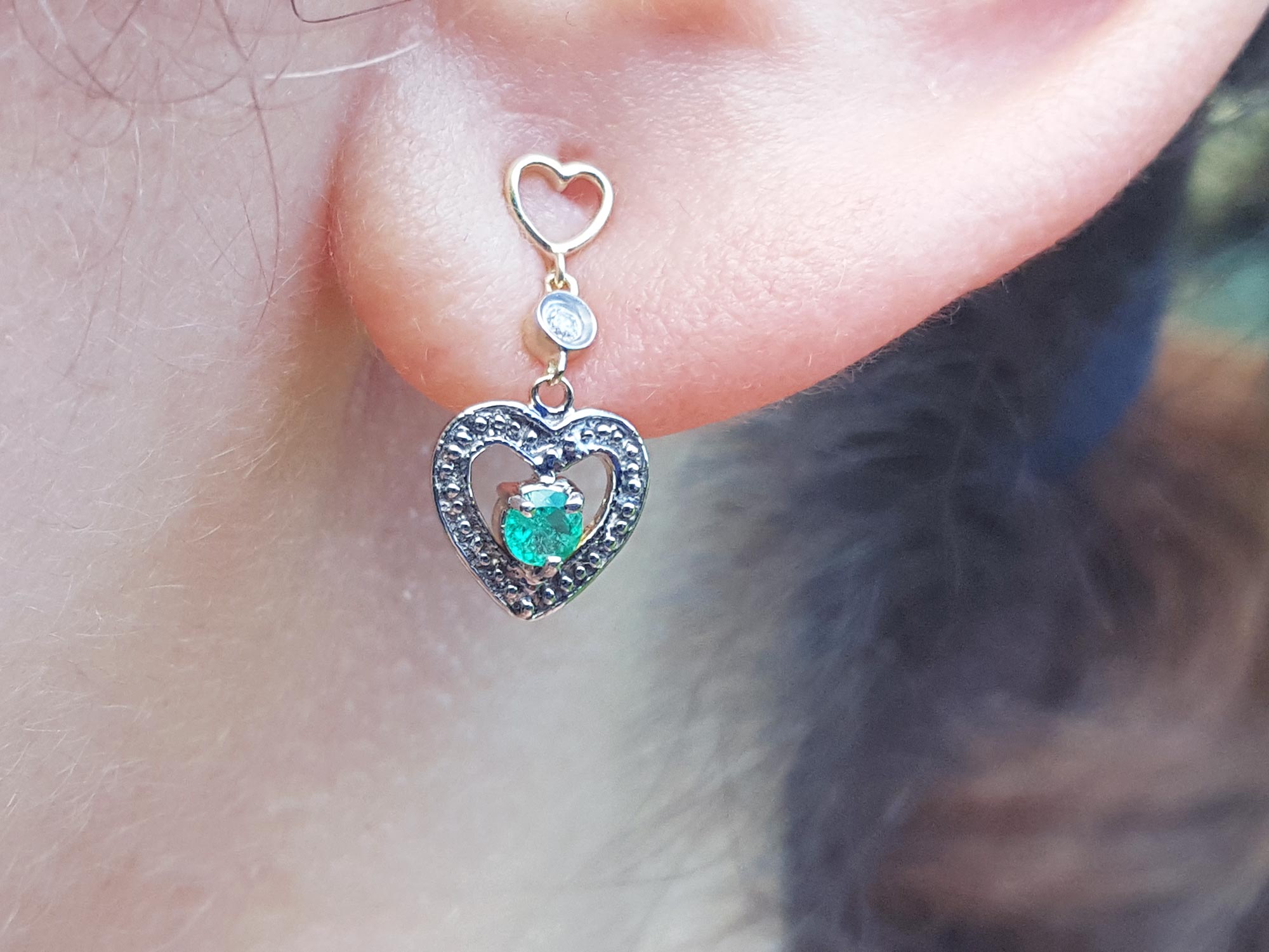 Emerald heart earring worn on a woman's ear, close-up view.
